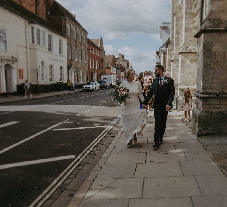 Urban portrait of bride and groom holding hands through the street 