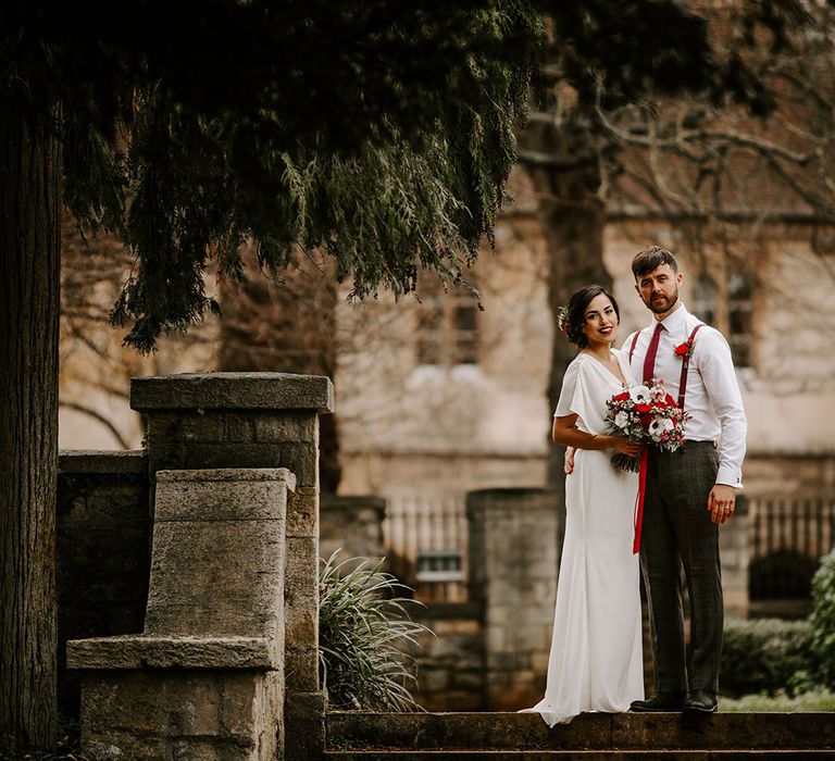 Bride with eucalyptus foliage bouquet stands with Groom in churchyard