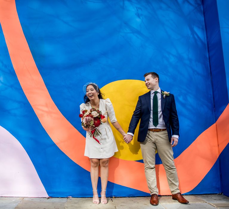 Bride and groom holding hands in front on a giant graffiti wall in Chelsea, London