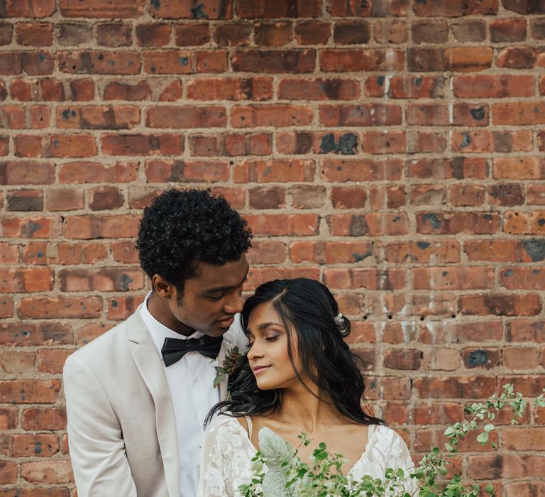 Groom in a grey jacket holding hands with his bride in an embellished wedding dress with white and wedding bouquet 