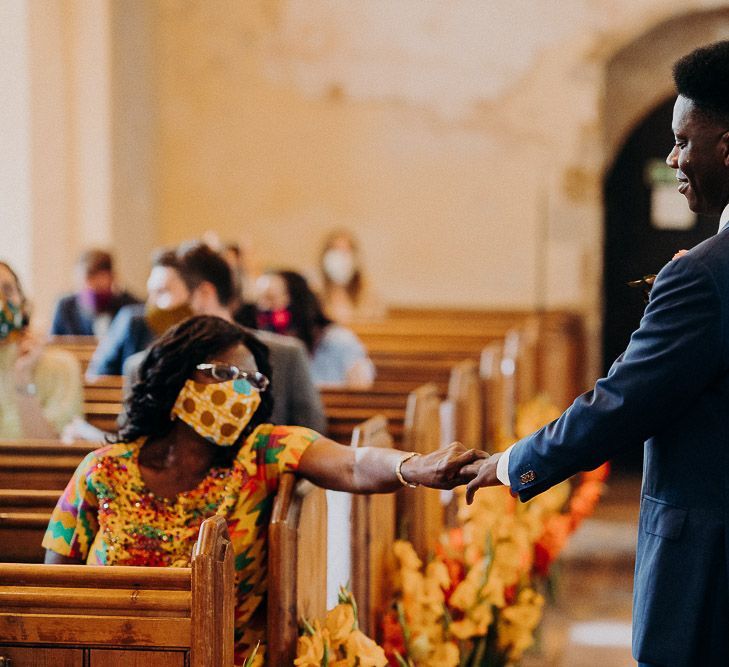 Groom in a navy suit at the church wedding altar holding his mums hand 