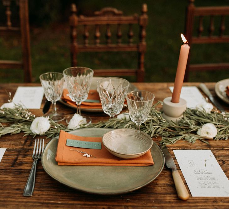 Place setting with green charger plate, orange napkin, foliage table runner, and taper candles 