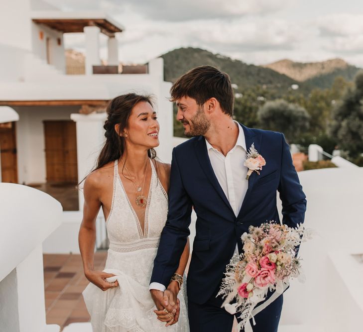 Bride in halter neck wedding dress holding her grooms hand in a navy suit at Ibiza villa 