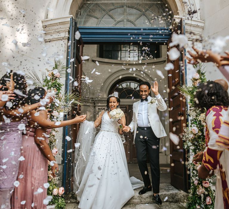 Confetti exit with the bride in a satin princess wedding dress and the groom in a white tuxedo jacket