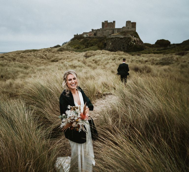 Bride walks through the grass whilst wearing shawl on the day of her wedding