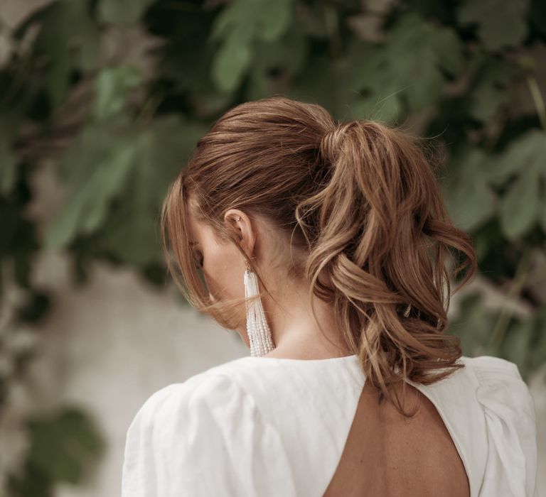 bride in a backless wedding dress with blouson sleeves with wavy ponytail and tassel earrings 