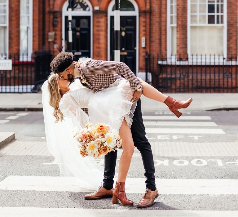 Groom in a patterned blazer leaning his bride down for a kiss in the street 