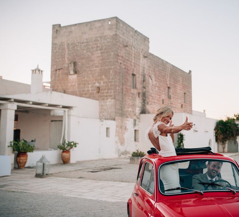 The bride standing through the sun roof of the vintage Fiat 500 wedding car