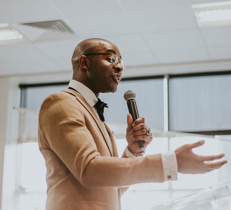 Pastor in camel suit jacket, white shirt and black bow tie holds microphone as he conducts wedding ceremony at Bridge Community Church