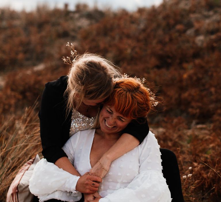 Same sex couple smiling and embracing in beach dunes