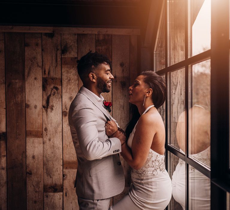 Bride & groom stand in front of window as the light streams through