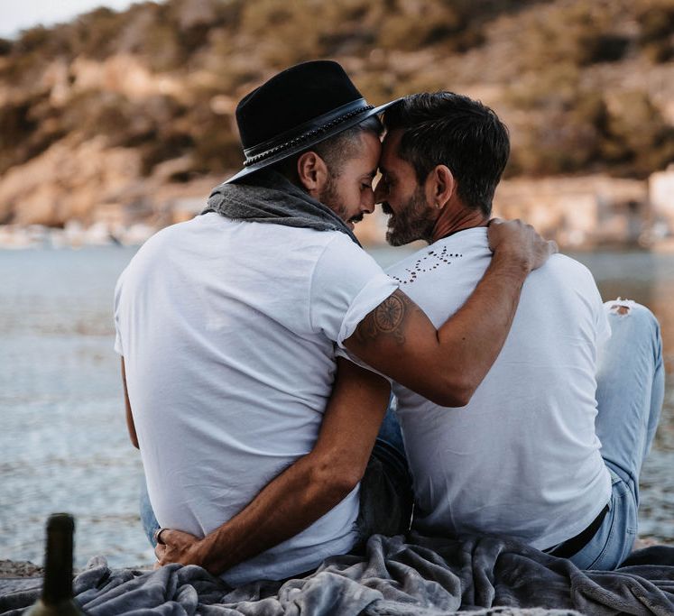 Grooms wrap arms around one another on the beach in Ibiza