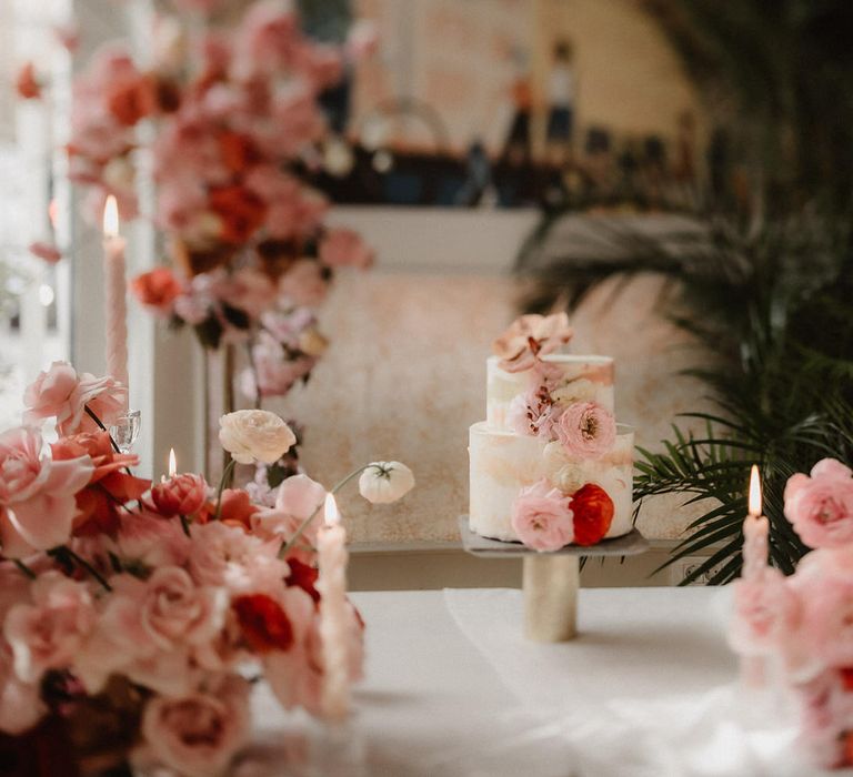 Two tier white wedding cake with brush effect detail, surrounded by pink wedding flowers and pink tapered candles