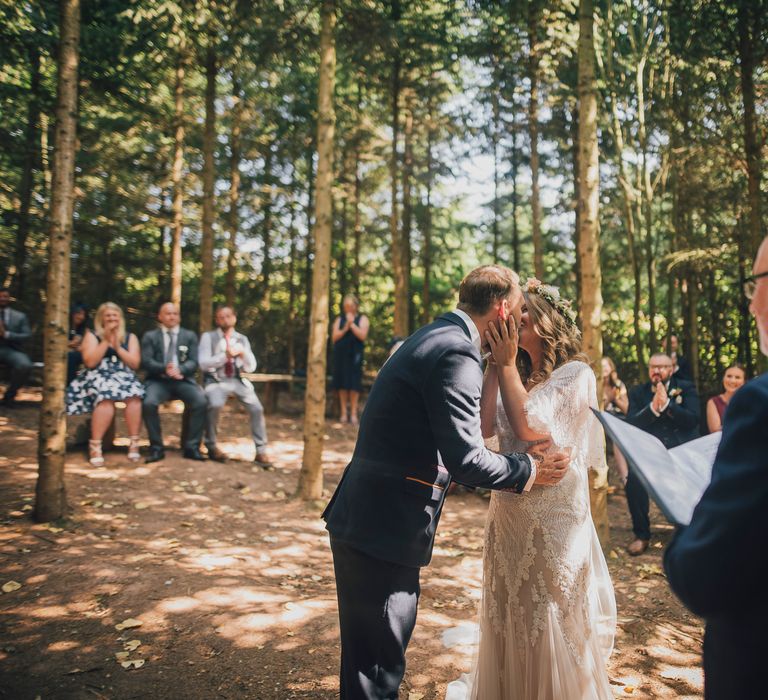 Bride & groom kiss during woodland wedding ceremony 