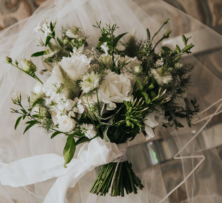 Brides floral bouquet filled with classic white flowers, green foliage, and tied with white silk ribbon