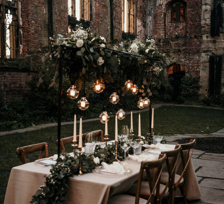 Outdoor wedding reception with festoon light installation and foliage table runner 