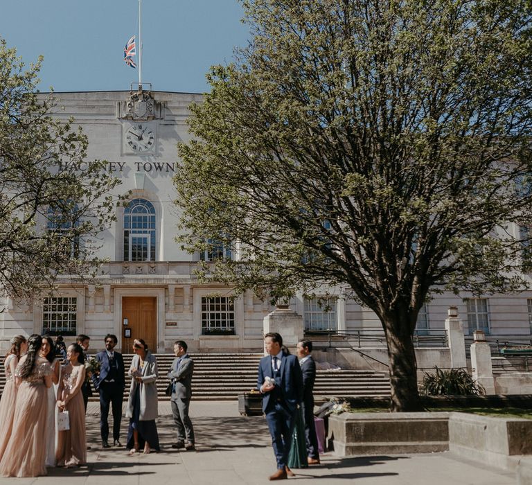 Micro wedding party guests mingle outside Hackney Town Hall in the sunshine