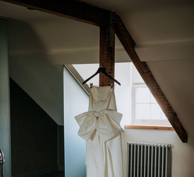 Strapless white Rebecca Vallance Dress with bow detailing on hanger in bathroom with two freestanding roll top baths at Hotel du Vin Harrogate for Harrogate wedding