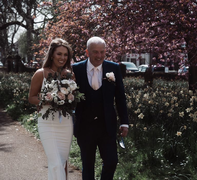 Bride wearing a white slip wedding dress walking to the church arm in arm with her father