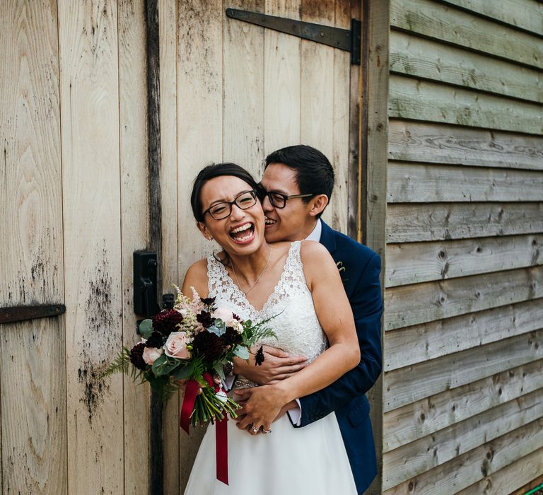 Groom embraces bride as he kisses her cheek on wedding day