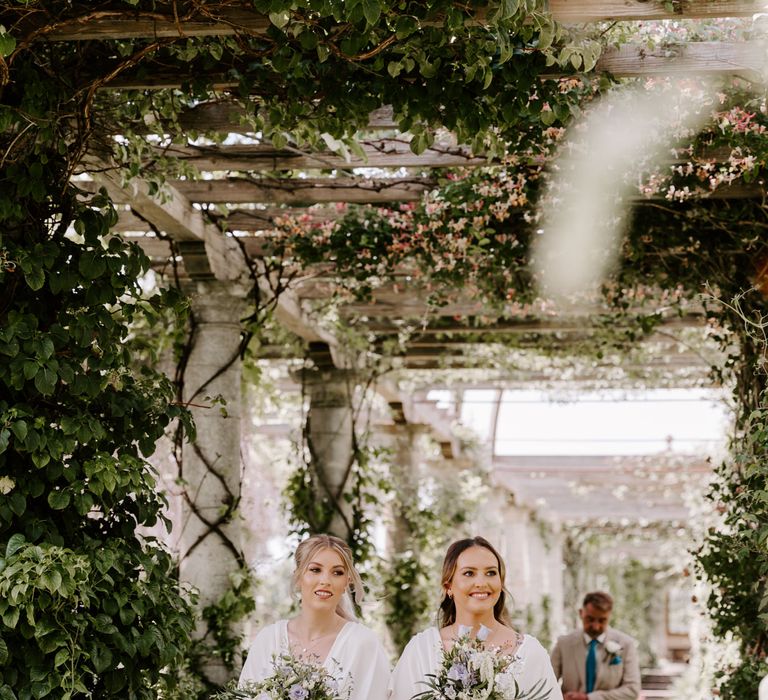 Bridesmaids walk through pergola in the gardens of West Dean Gardens 