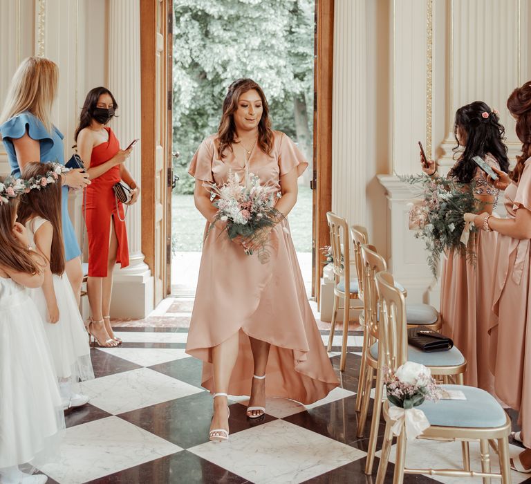 Bridesmaid walks down the aisle wearing silk peach coloured dress from Missguided 