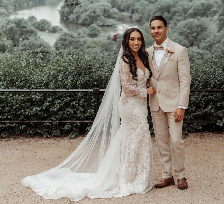 Bride & groom stand outdoors on their wedding day as the brides veil blows to the side of her