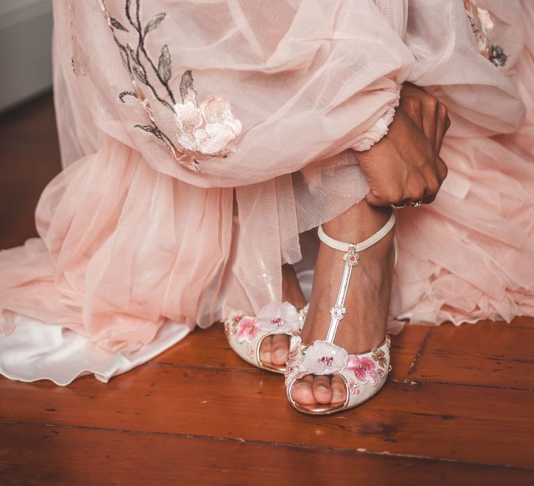 Bride in a blush pink dress leaning down to put on her peep toe T-bar wedding shoes 