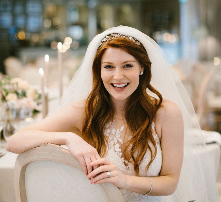 Classic bride with long wavy hair wearing a wedding veil sitting on an ivory Louis chairs at the Grantley Hall wedding reception 