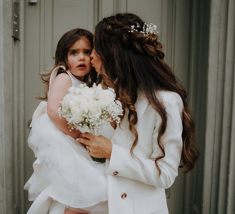 Bride in a trouser suit holding her daughter and a white rose bouquet 