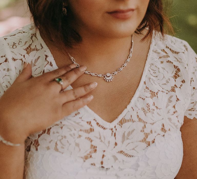 Indian bride with shoulder length hair in a lace wedding dress touching her silver necklace 