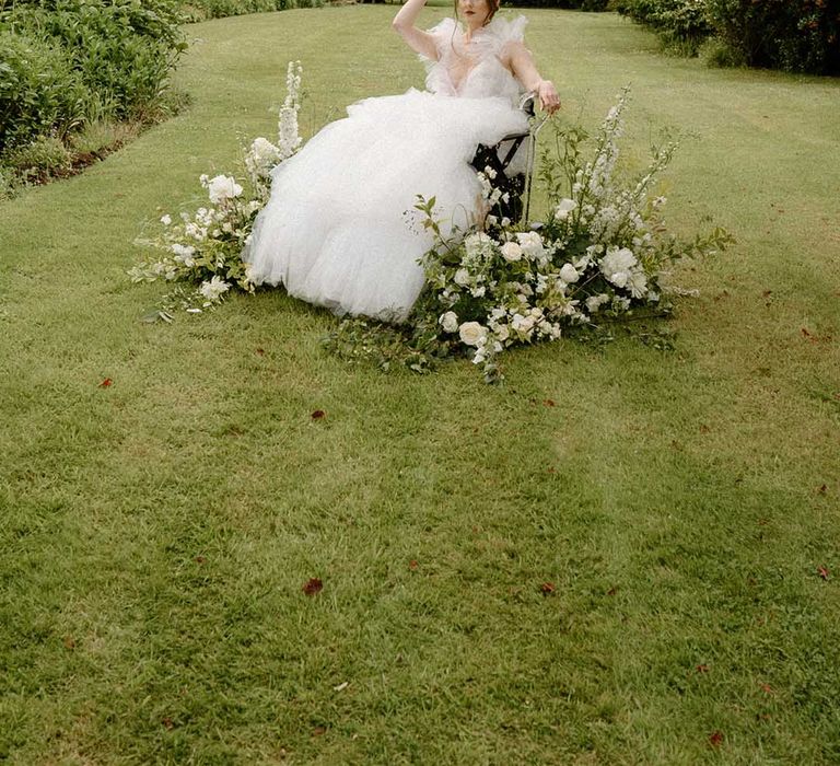 Beautiful bride in a wheelchair sitting in the gardens at Bourton Hall surrounded by white and green floral arrangements 