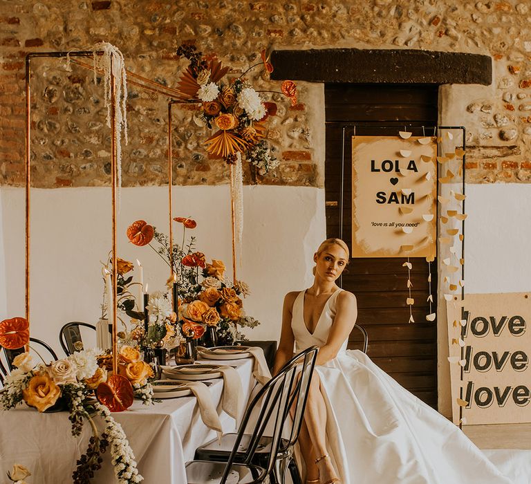 Bride in a Jesus Peiro wedding dress sitting at a contemporary table decorated with black accents and yellow and orange wedding flowers 