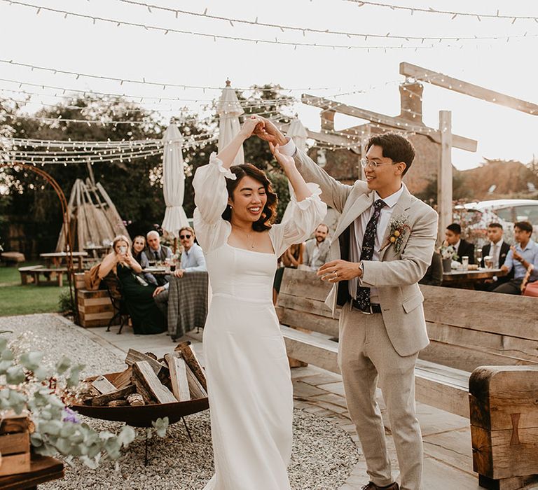 Bride & groom dance outdoors in front of fire pit as wedding guests watch