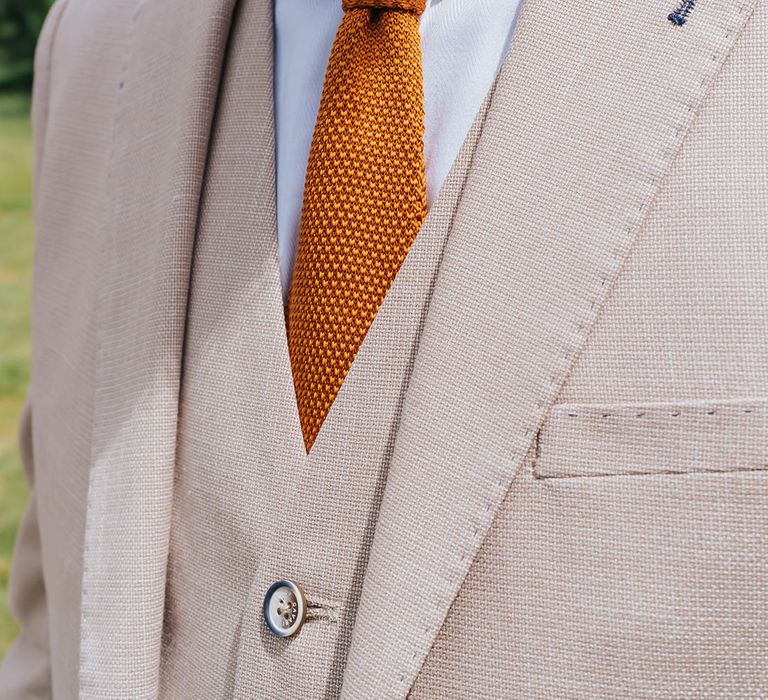 Groom in a beige three-piece suit with white shirt and orange waffle tie