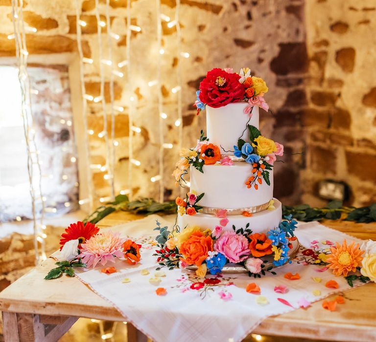 White three tier wedding cake with multicoloured floral decorations on wooden table at The Bridal Barn wedding reception