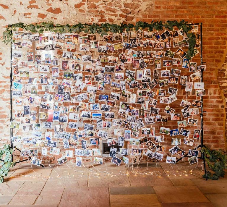 Large fairy light wedding photo wall with leaf garland surround for rustic barn wedding