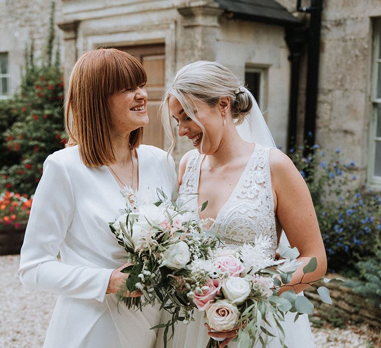 Brides laugh together as they clutch blush bouquets