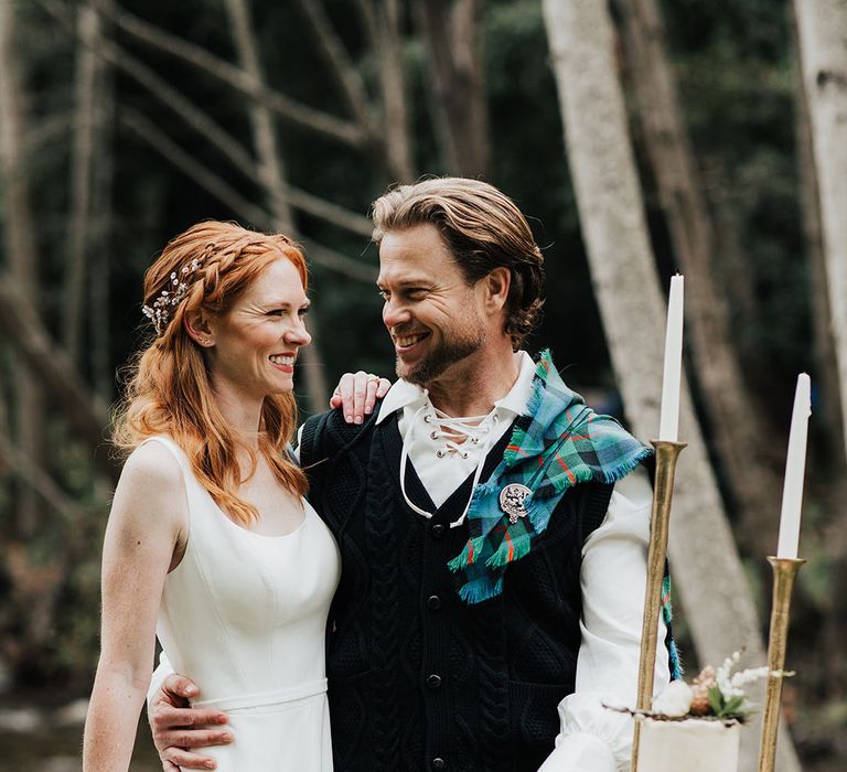 Groom in a kilt, sporran and aran embracing his bride with red hair in a princess wedding dress 