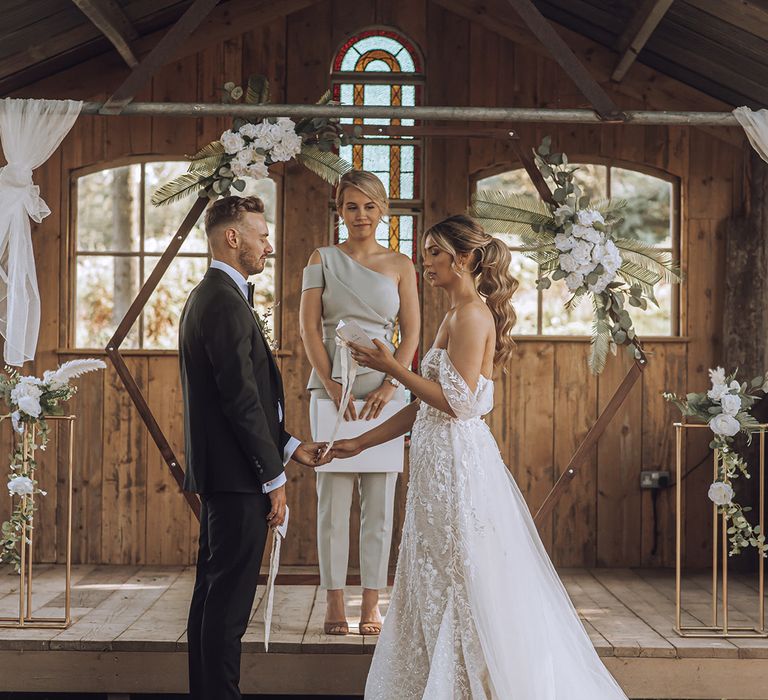 Bride & groom stand within outdoor barn on their wedding day during ceremony