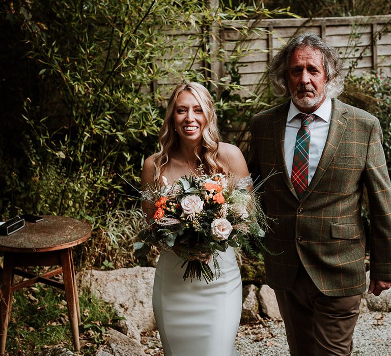 Bride walks with her father who wears tartan blazer 