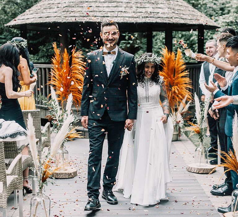 Bride walks down the aisle in front of bright orange pampas grass as wedding guests throw confetti around them