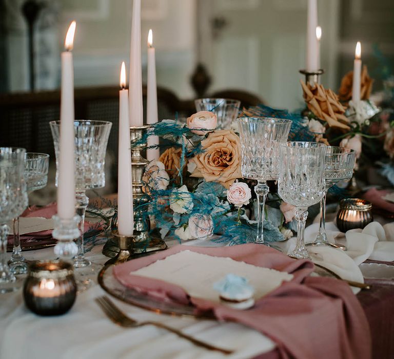 Luxury wedding table decor with glass goblets, gold candlesticks and pink taper candles, plus pink linens and romantic flower centrepiece 