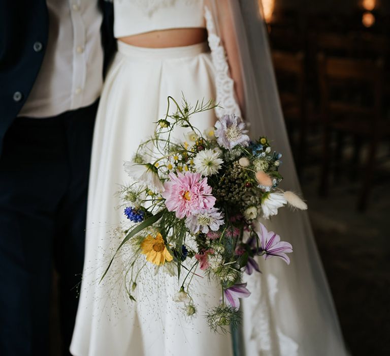 Bride holding colourful wedding bouquet of assorted flowers wearing pleated high low skirt