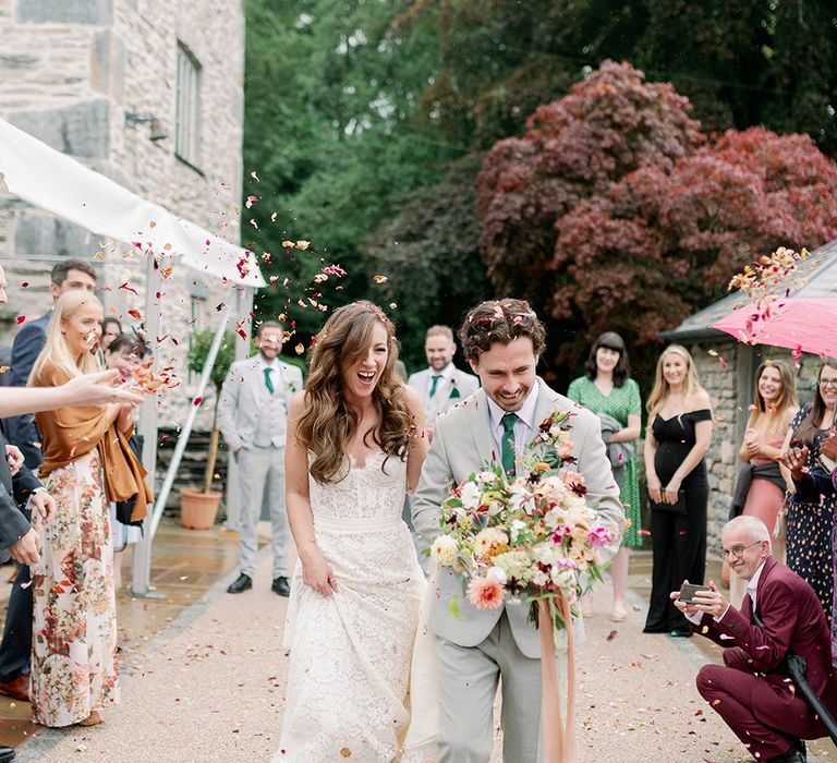 Bride in strapless lace wedding gown and green pointed heels with groom in light grey suit and matching green tie walk through confetti 