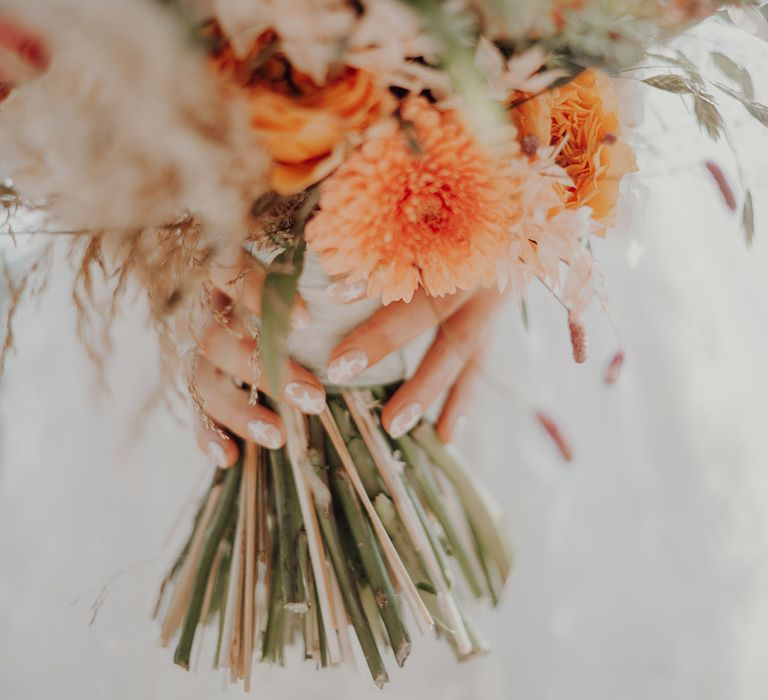 Bride's white star wedding nails holding orange autumnal wedding bouquet