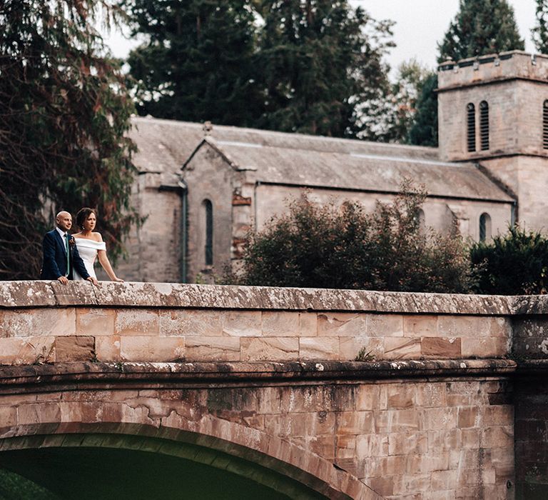 Bride and groom stand on a bridge and look out at the view at Askham Hall wedding venue