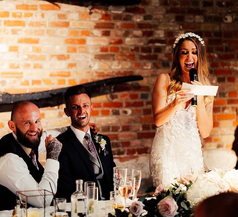 Bride gives a bridal speech at her wedding seated on top table with groom and best man 