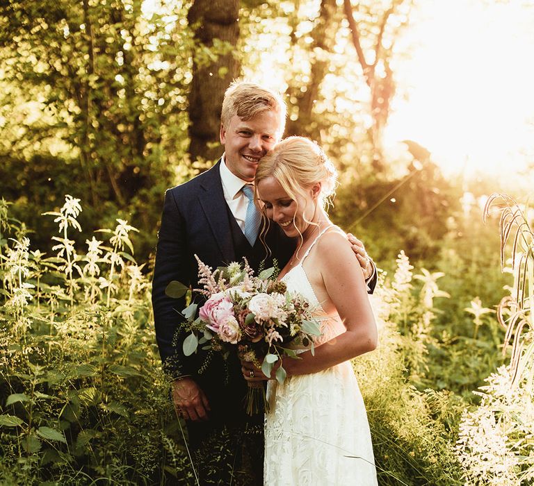 Groom in blue suit with light blue tie holding bride in boho lace wedding dress with pink wedding bouquet