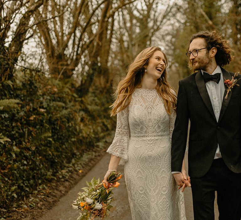 Laughing bride in full lace a-line Rosa Clara wedding dress with bell sleeves and groom in black tie